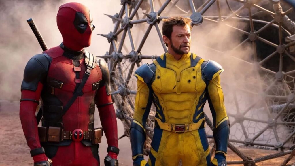 The image features two characters standing side by side. On the left is a character in a red and black suit with a mask, representing Deadpool. On the right is another character in a yellow and blue suit with their face obscured, intended to represent Wolverine. They appear to be standing on rocky terrain with sparse vegetation in the background. This image may be relevant for fans of comic book characters or movies, showcasing two popular Marvel characters known for their distinctive costumes and association with the X-Men series. This is the Deadpool & Wolverine movie review
