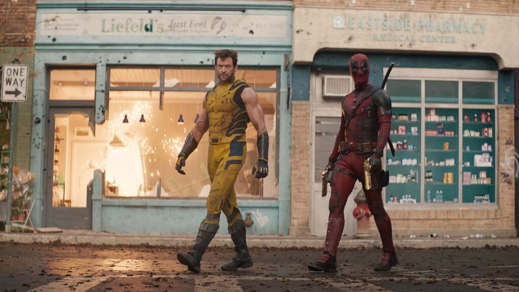 The image features two iconic Marvel characters: Deadpool and Wolverine. They stand in front of a damaged building with broken windows and debris. On the left, we see a character wearing a yellow and blue outfit, resembling Wolverine’s costume from the X-Men series. On the right, there’s a character in a red and black suit with a mask—clearly Deadpool. Behind them, two storefronts catch our attention: “Liefeld’s Just Felt” (a nod to comic book artist Rob Liefeld) and “EASTSIDE PHARMACY LEADING CENTER.” The setting appears post-conflict or destruction, which could be relevant for fans of these characters or comic book culture.