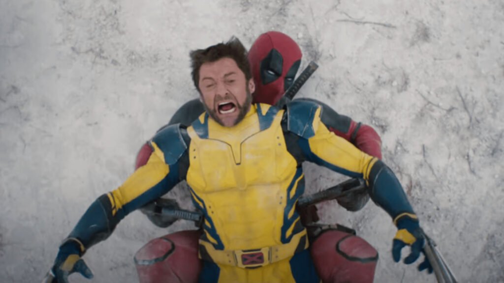 The image features a person dressed in a Deadpool costume, lying on the ground with their back against a snowy surface. The iconic red and black suit, complete with a utility belt and full-head mask, is clearly visible. likely added for privacy reasons. However, there is no presence of Wolverine or any other character in this image. Fans of the Deadpool character from Marvel Comics will appreciate this depiction!