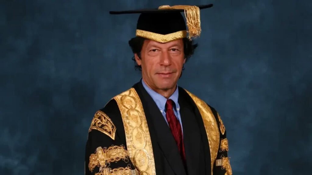 The image shows Imran Khan wearing academic regalia, which includes a black mortarboard (graduation cap) and a black gown with gold embellishments on the sleeves and front. He is also wearing a red tie and a white shirt under the gown. The background is a solid dark blue color.