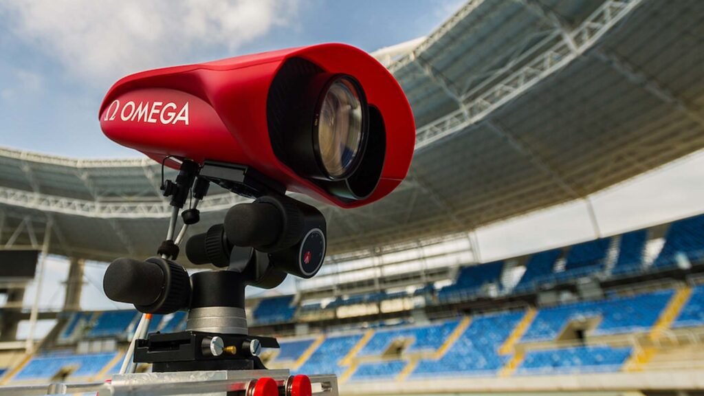 A Red Omega starting block camera system positioned at a track and field stadium, capturing high-resolution footage to monitor athletes’ starts during competitions. The empty stadium seats in the background suggest a practice session or preparation for an upcoming event.