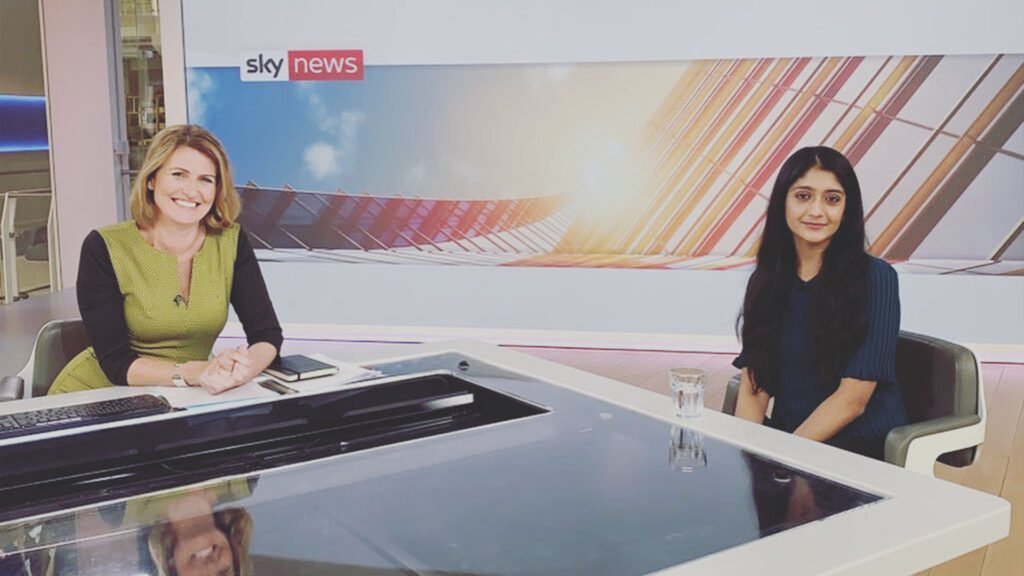 The image shows Laraib Atta, a Pakistani visual effects (VFX) artist, during an interview at a Sky News studio. She is seated at a desk across from an interviewer, with the Sky News logo visible in the background. Laraib is dressed in black, and the interviewer is in a green outfit.
