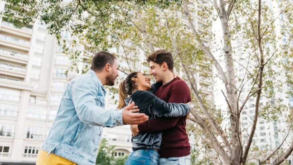 Three individuals embracing in a group hug, showcasing symbiosexuality, with a blurred urban background.