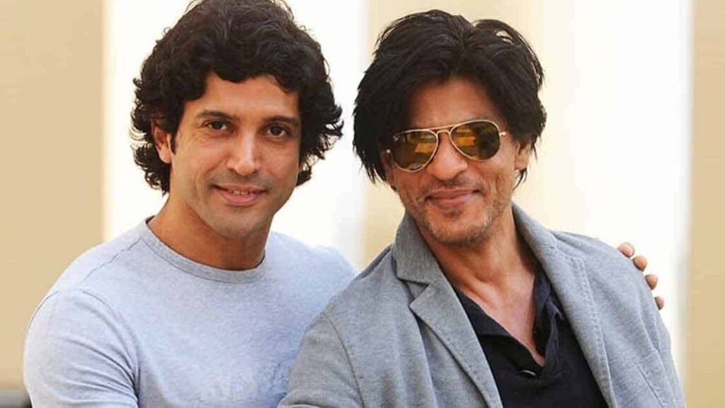 Shah Rukh Khan (SRK) and Farhan Akhtar standing close to each other, with one placing their arm around the other’s shoulder in a friendly manner. Both are dressed casually; the person on the left is in a light grey t-shirt, and the person on the right is wearing a black shirt with a dark blazer. This image conveys a sense of camaraderie and friendship, suitable for a website featuring Shah Rukh Khan (SRK) and Farhan Akhtar.