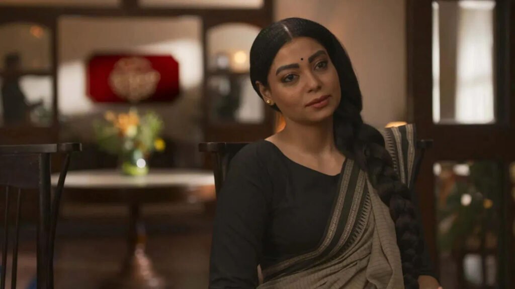 The character Zarina from ‘Mirzapur,’ seated in a traditional setting with the series’ logo subtly visible in the background.
