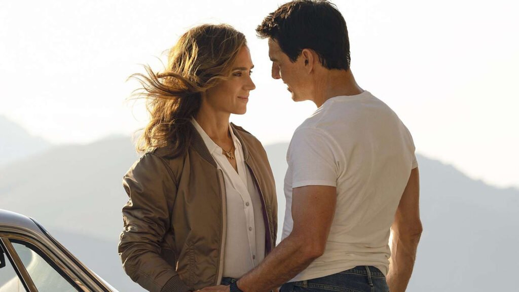 Jennifer Connelly young and Tom Cruise standing side by side with a scenic mountain backdrop, suggesting a still from a film or public appearance.