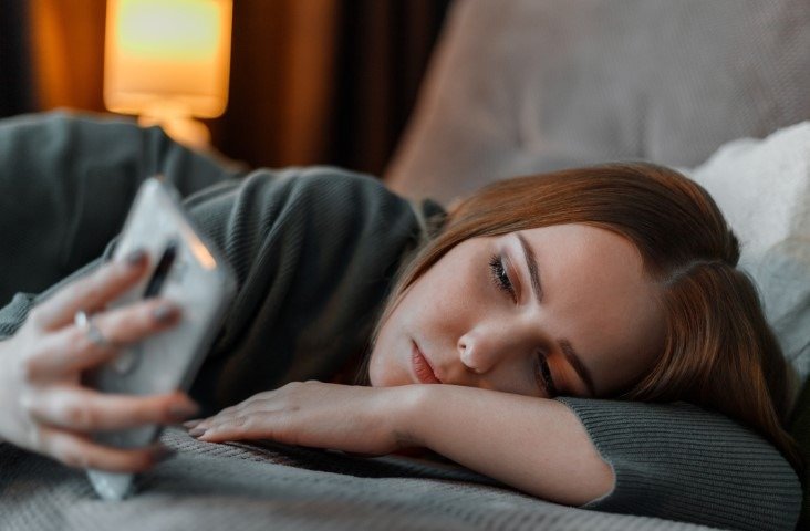 A Gen Z girl lying on a bed and scrolling phone.