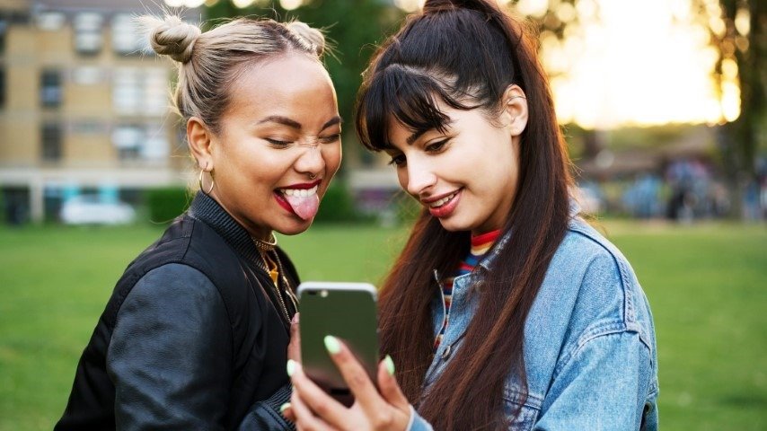  Two Young Gen Z girl taking selfie on their phone. with a greenery and beautiful sunny day