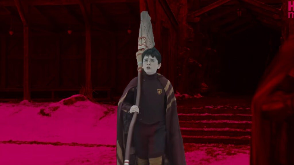 No Cap, the Harry Potter Trailer Just Reset the Entire Wizarding World 7 A cinematic production still from the HBO Harry Potter reboot. Dominic McLaughlin stands in the foreground, pale-faced and wearing a dark red and gold Gryffindor Quidditch robe while holding a tall broomstick. The background features a snowy, outdoor setting under a heavy magenta and deep red color grade, showcasing the high-contrast, moody visual language of the new series.