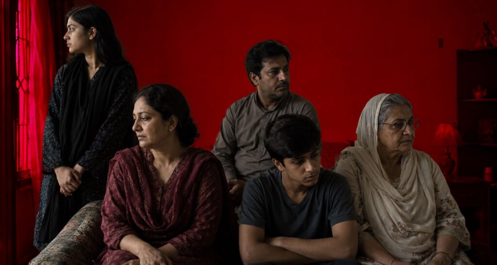 The picture should depict a family scene where several generations have gathered. They should all be standing close to one another, but there seems to be an emotional disconnect between them. They are clearly related through blood ties but lack emotional connection.