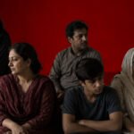 The picture should depict a family scene where several generations have gathered. They should all be standing close to one another, but there seems to be an emotional disconnect between them. They are clearly related through blood ties but lack emotional connection.